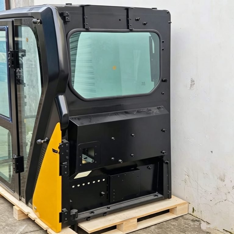 Black and yellow excavator cab assembly with glass and open door on a shipping pallet
